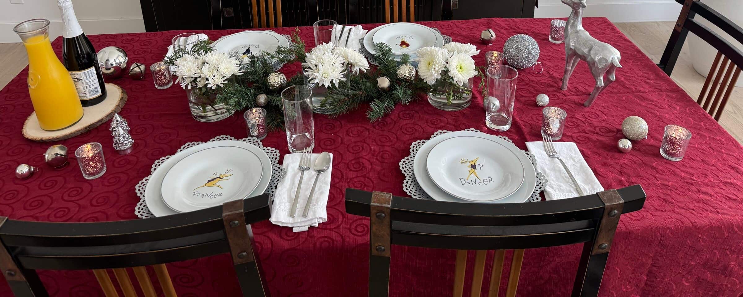 An at-home Christmas dinner table set with reindeer place settings, a white floral and pine centerpiece, and a nutcracker collection