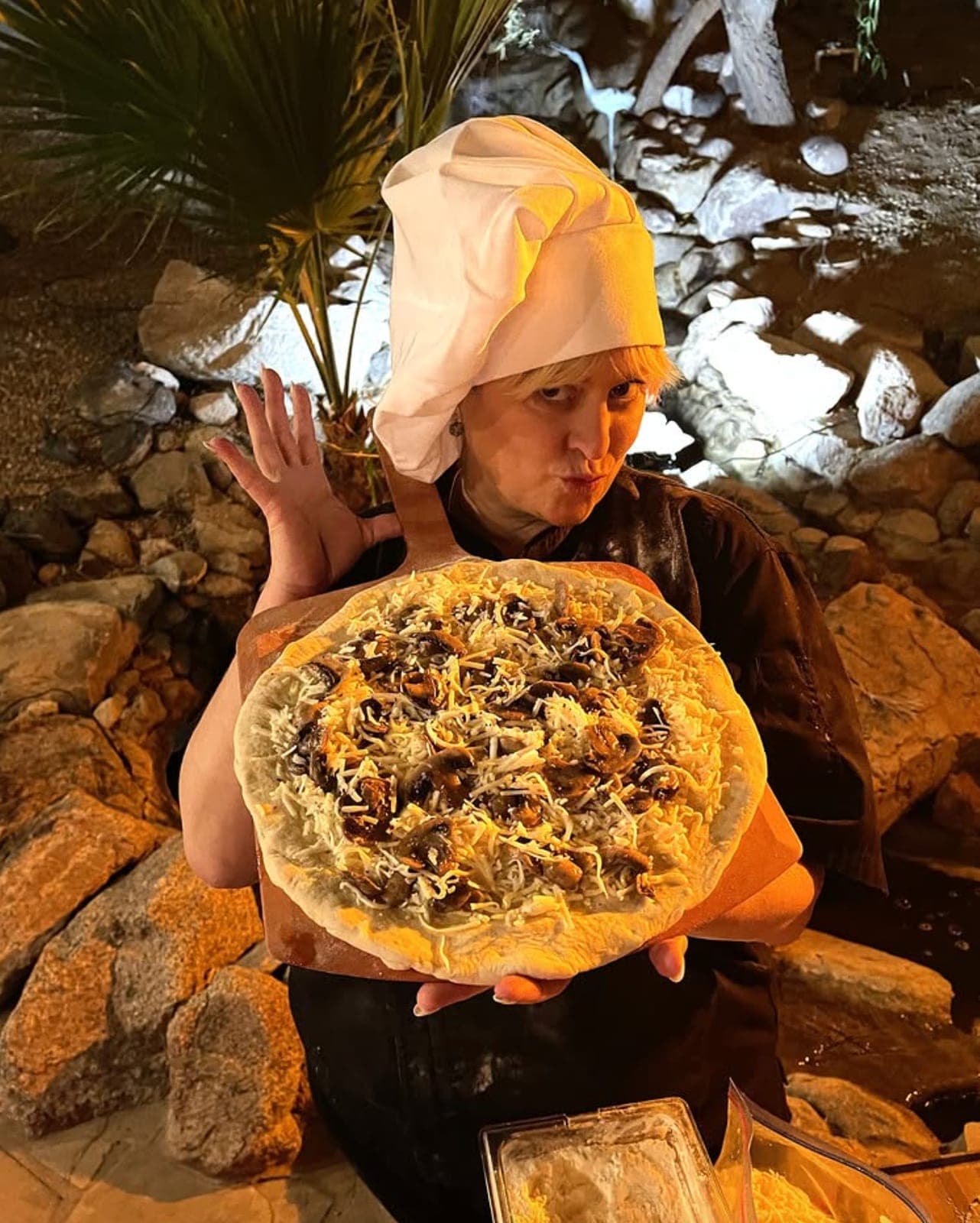 Emily in a chef's toque presenting a large hand-stretched pizza
