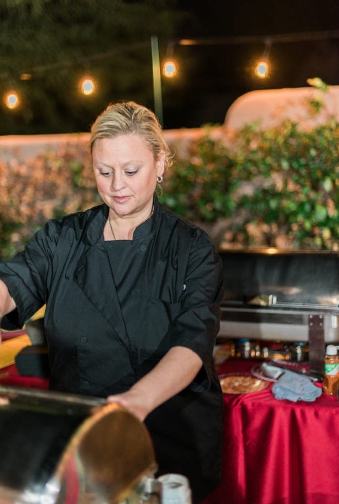 A chef in uniform working a buffet station under string lights