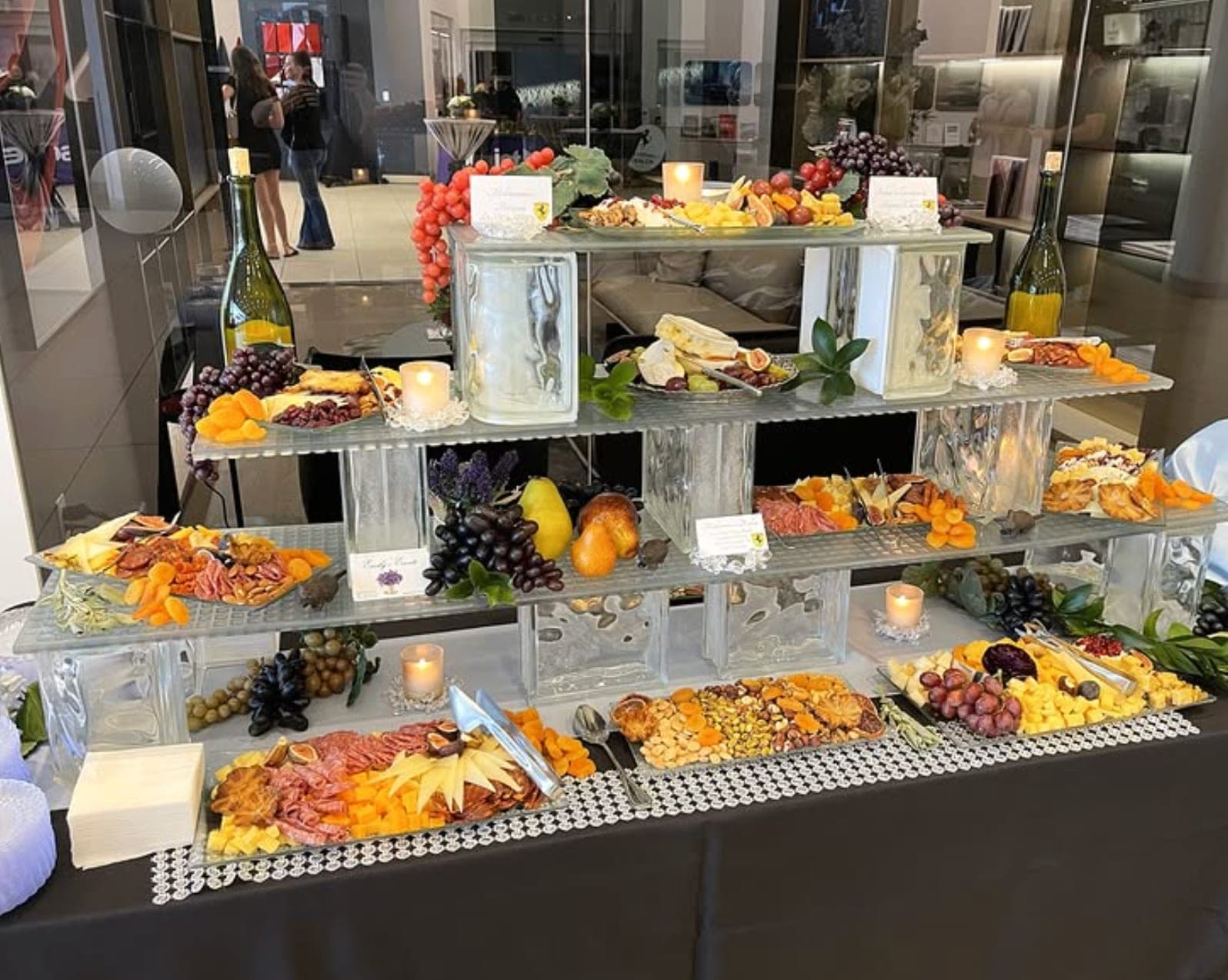 A tiered grazing display of charcuterie, cheeses, fruit, and candles on glass risers