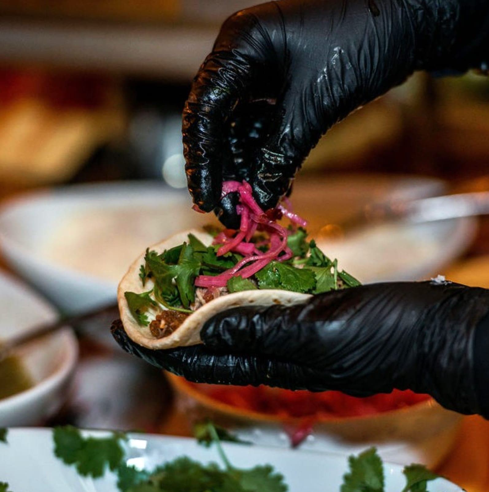A chef finishing a street-style taco with cilantro and pickled onion