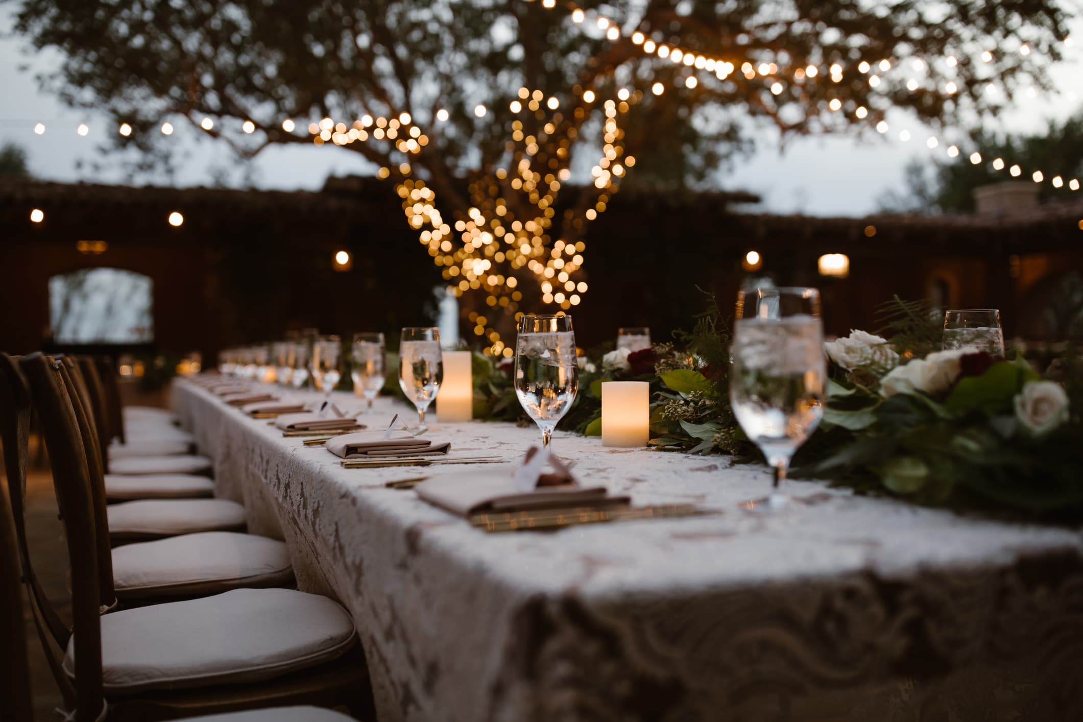 Long outdoor reception table at dusk strung with warm lights