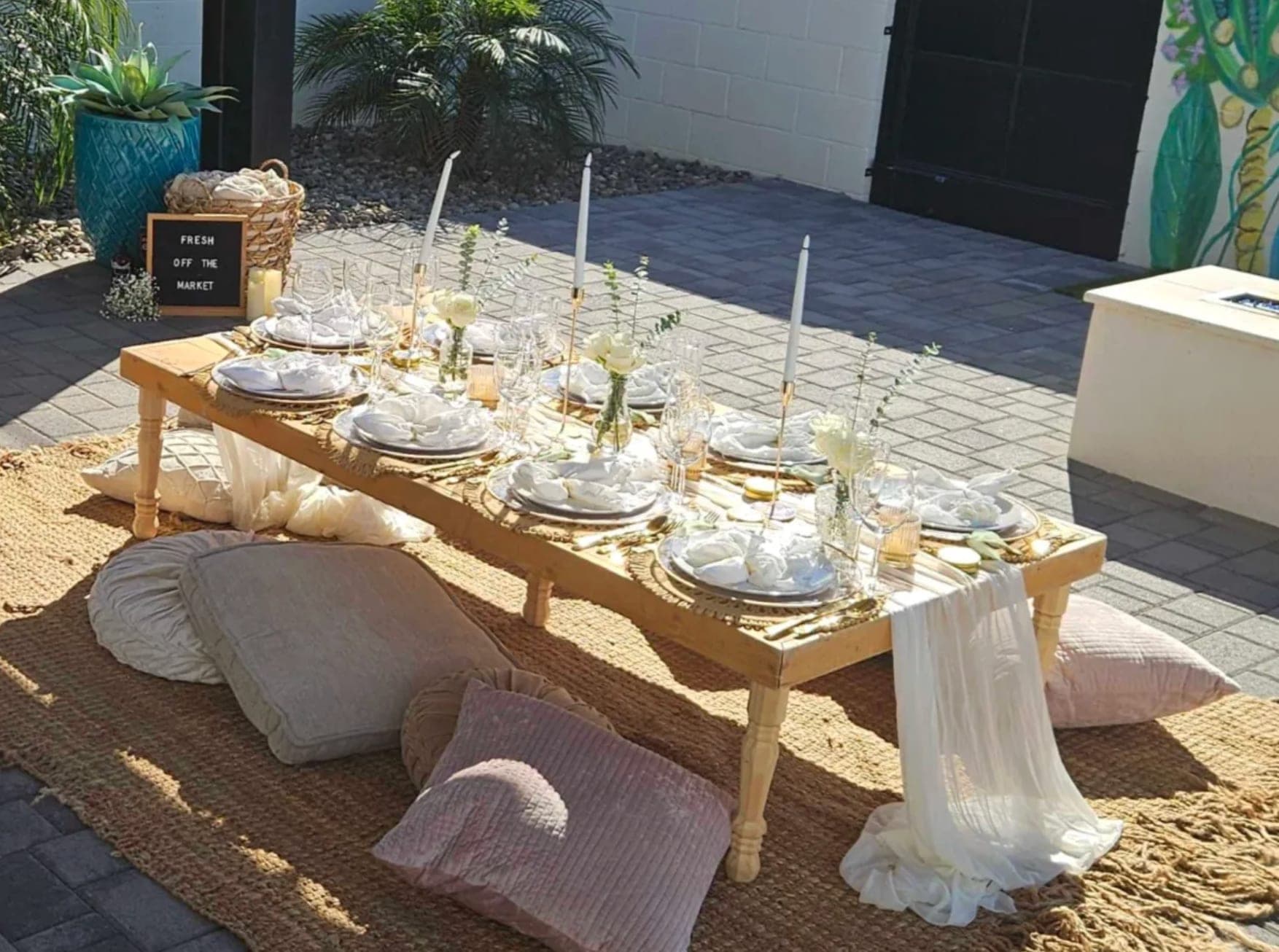 A styled low picnic table with rental place settings, glassware, and cushions